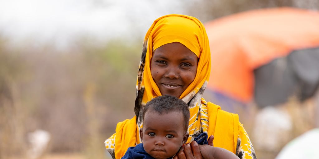 Abay Osman, 32-year-old mother of 6 holds her youngest son Hamza, 7 months outside their shelter in Dadaab