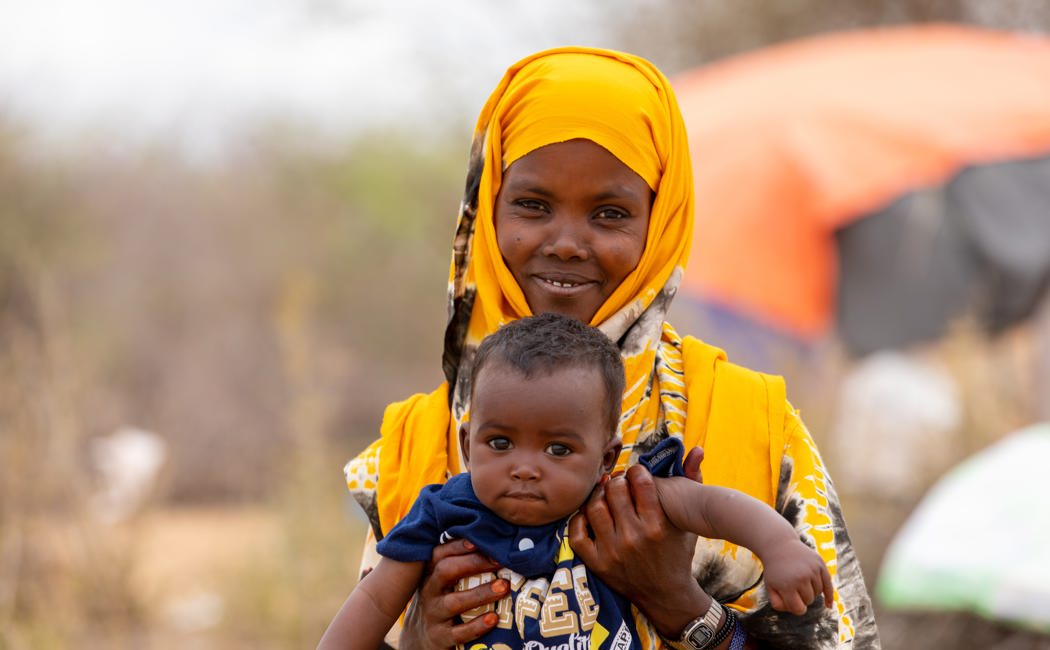 Abay Osman, 32-year-old mother of 6 holds her youngest son Hamza, 7 months outside their shelter in Dadaab
