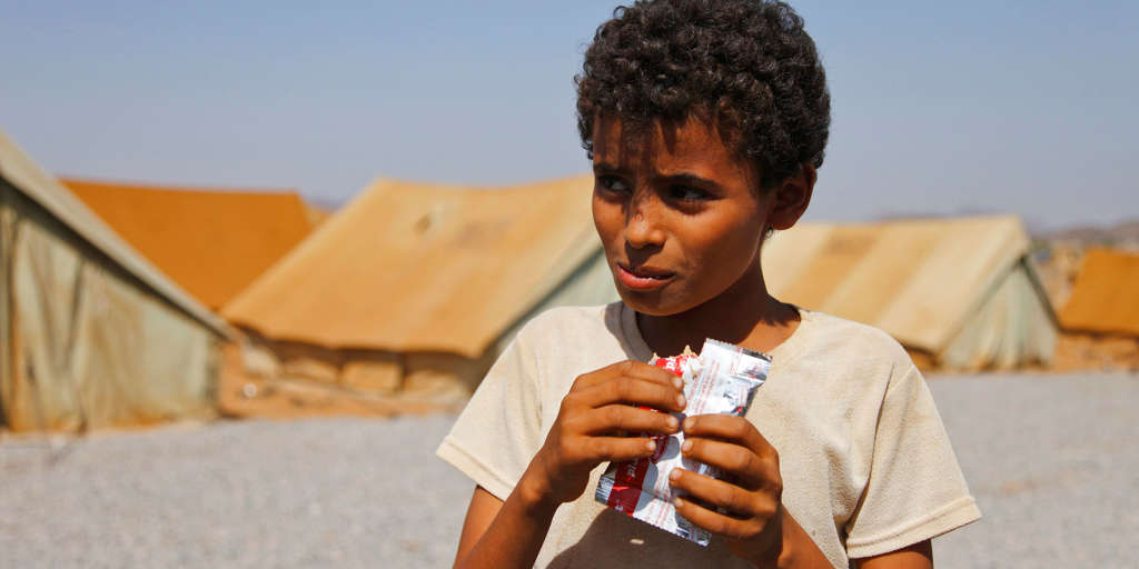 A young Yemeni boy in Mazrak IDP camp eats from a satchet of 'Plumpy'nut', a peanut-based food used in famine relief