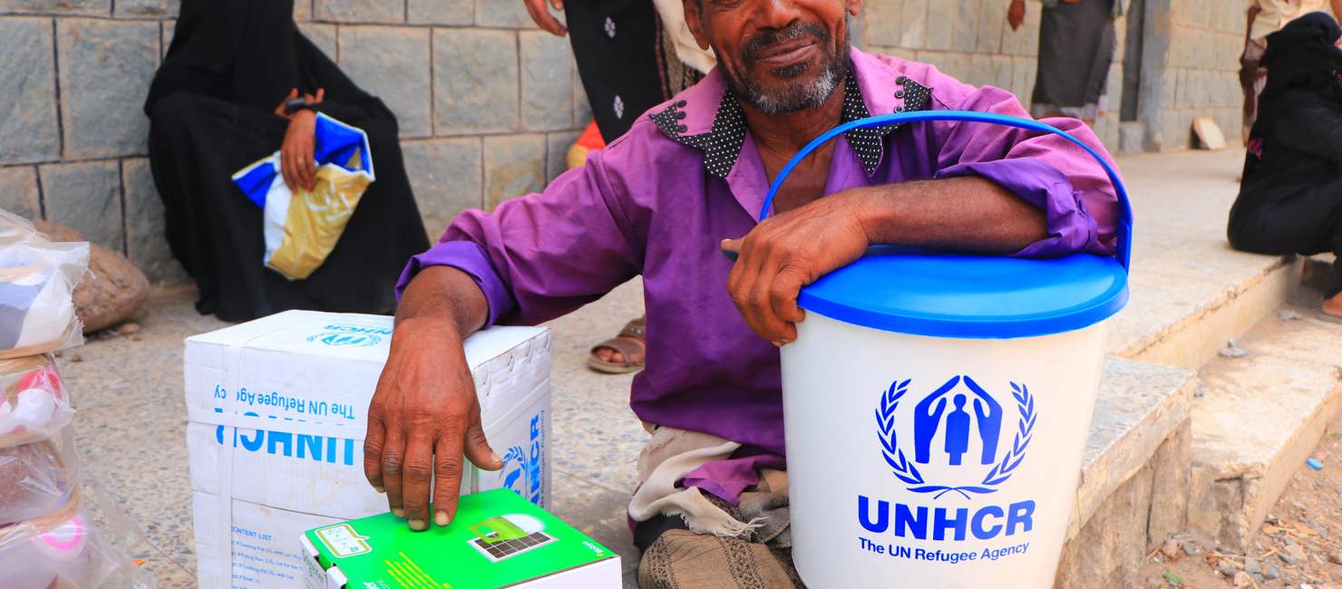 Man with UNHCR supplies looks at camera. Displaced families in Yemen receive essential household items.