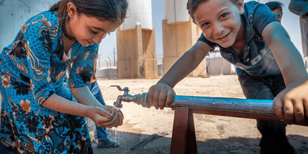 Two young children smile next to a tap with fresh water flowing