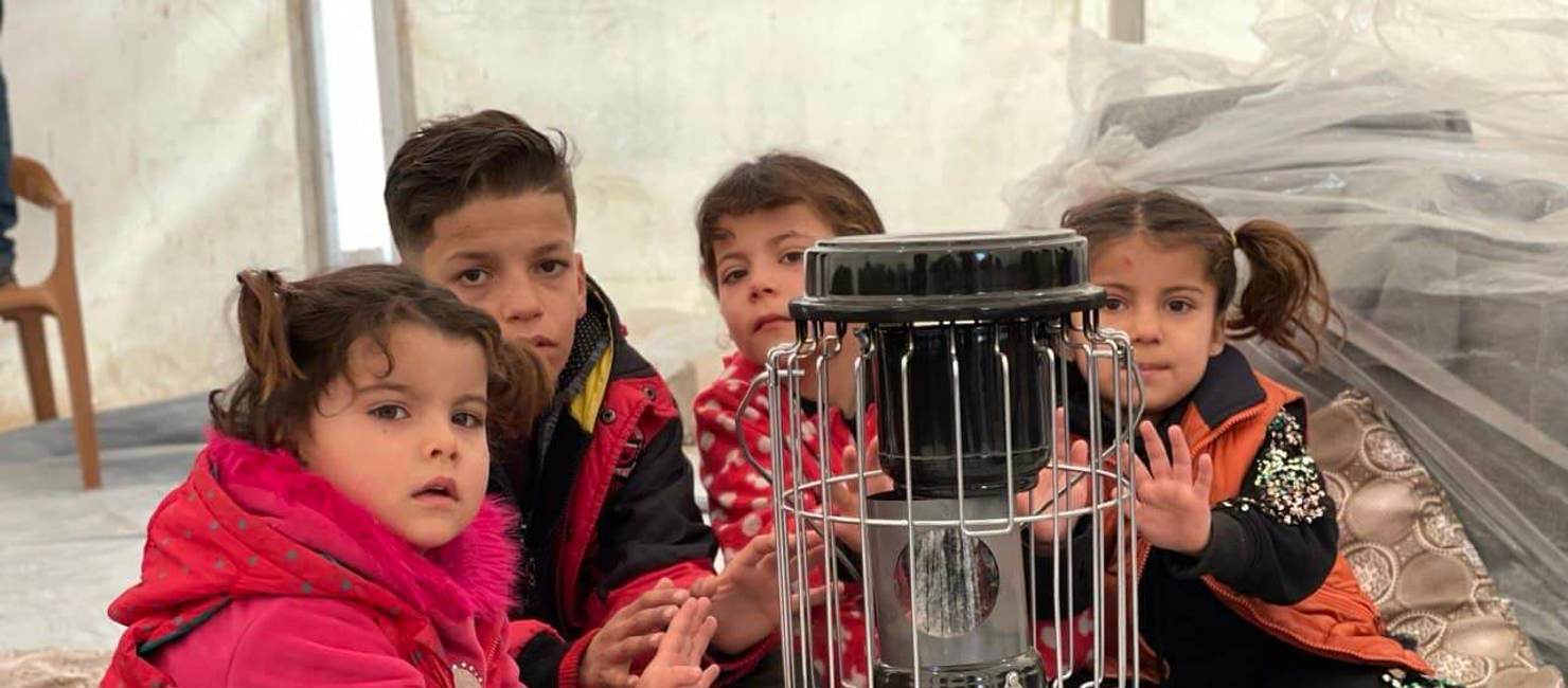 Syrian refugee children warm themselves on a kerosene heater in Bardarash refugee camp, near Duhok in Iraqi Kurdistan.