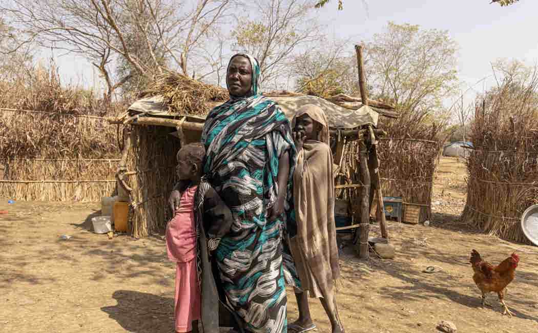 Hawa, 40, and her daughters Islam, 7, and Maha, 10, stand in front of their shelter at the Kurmuk transit centre, Ethiopia.