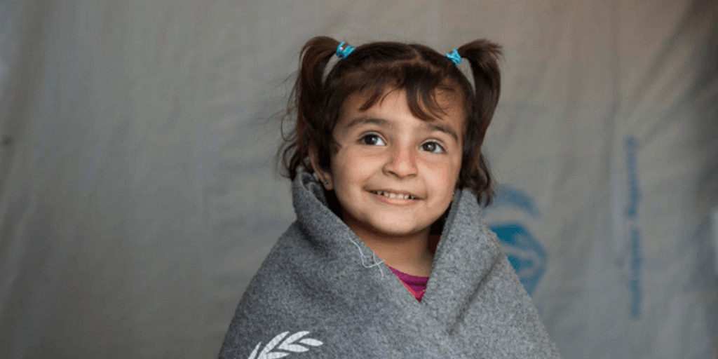 Small refugee child huddles under warm UNHCR blanket 
