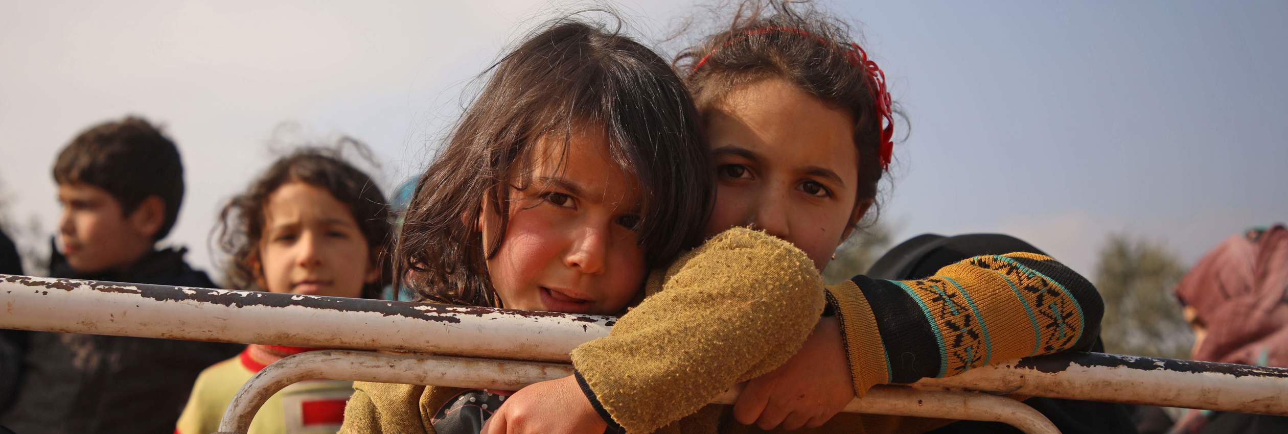 Displaced Syrian girls stand in the back of a truck parked at a newly-established camp on the edges of Maaret Misrin town in Syria's Idlib province