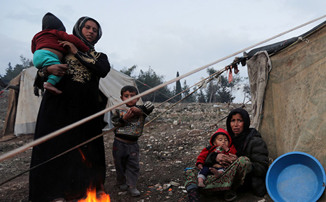 A Syrian woman and her children gather around a fire after fleeing southern Idlib
