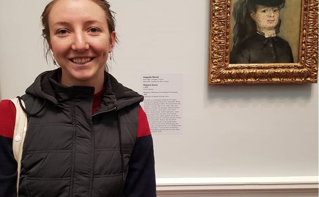Sophie Forest stands in front of impressionist artwork 