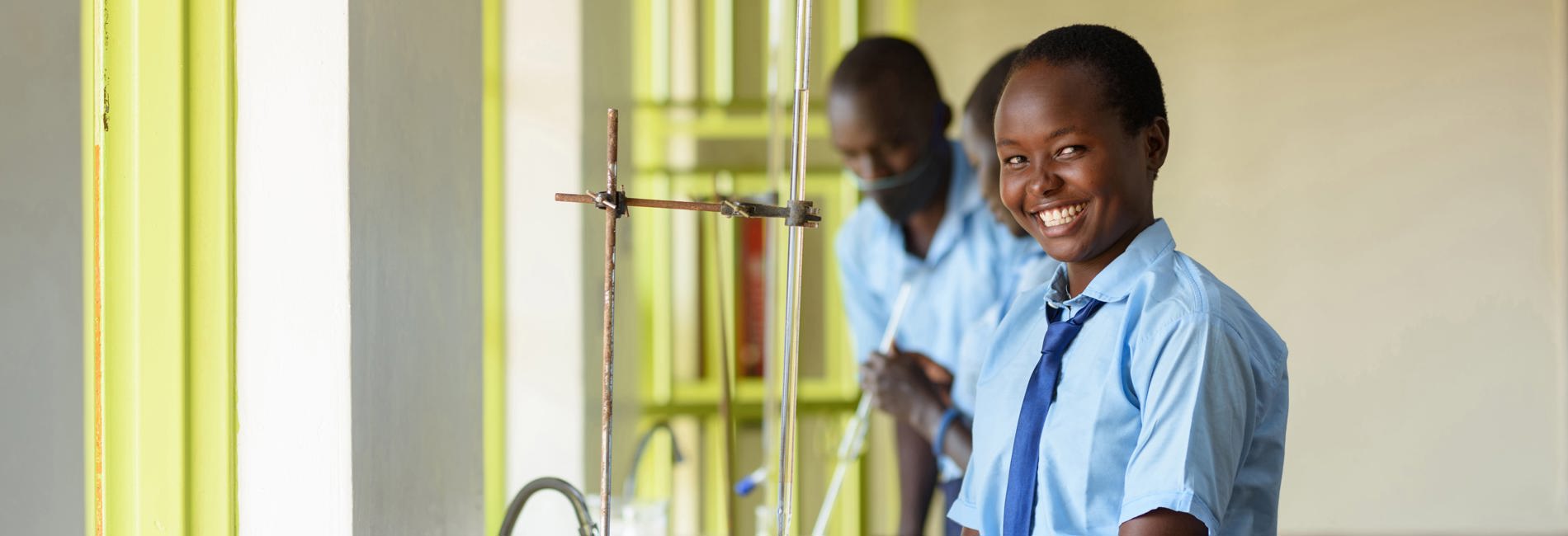 Young girl in school uniform smiles at camera. South Sudanese refugee, Sophie during a chemistry class in Uganda. 