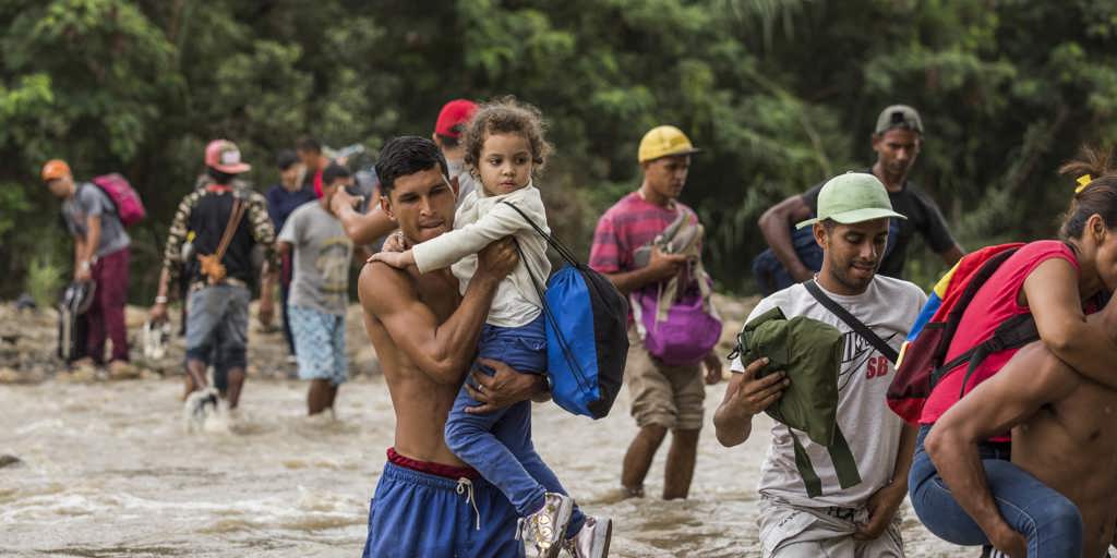 A father carries his young daughter through treacherous, muddy scrublands by the banks of the Tachira River, which forms the border between Venezuela and Colombia. In a context of rampant hyperinflation, food shortages, political turmoil, violence and persecution, more than 3 million Venezuelans have fled the country, making such perilous journeys in search of safety. 