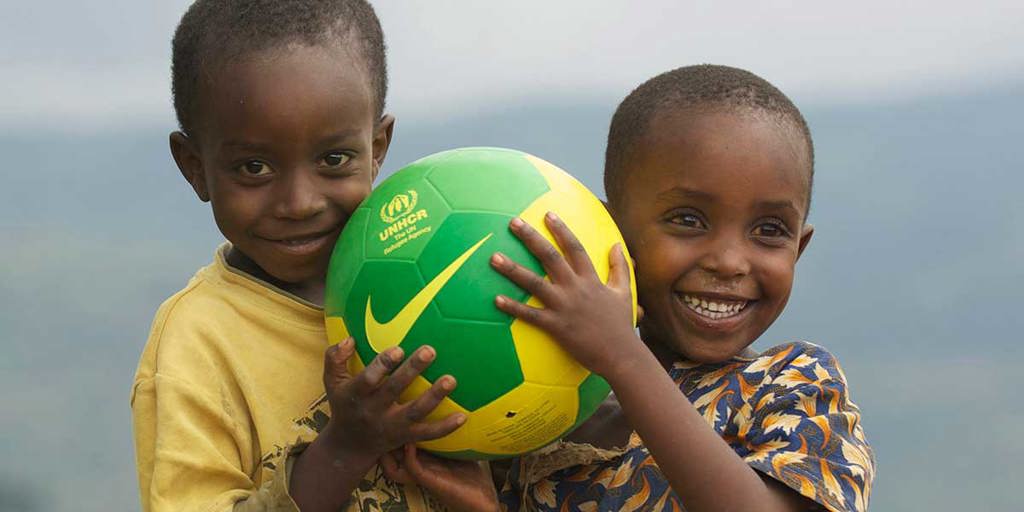 Two young children hug a soccer ball, smiling. 