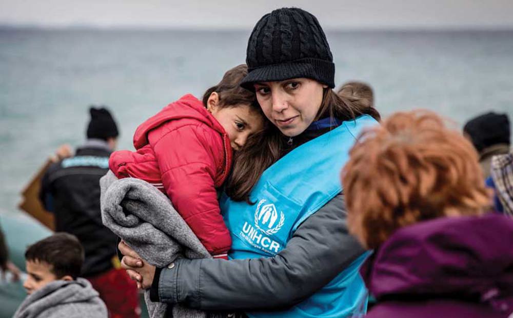 A UNHCR staff member holds a young refugee boy in a blanket, after his boat landed on the Greek island of Lesvos.