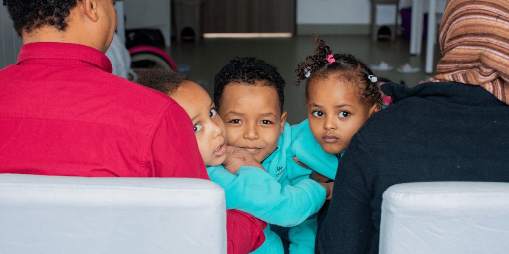 Three Eritrean children peek at the camera from their parents' laps