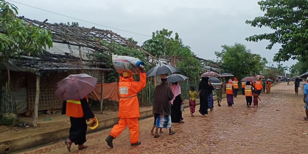 Volunteers help Rohingya refugees evacuate from their shelters as the rain falls
