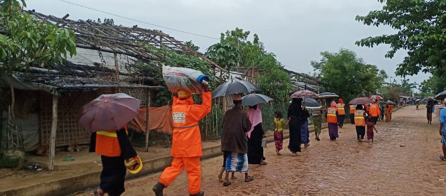 Volunteers help Rohingya refugees evacuate from their shelters as the rain falls