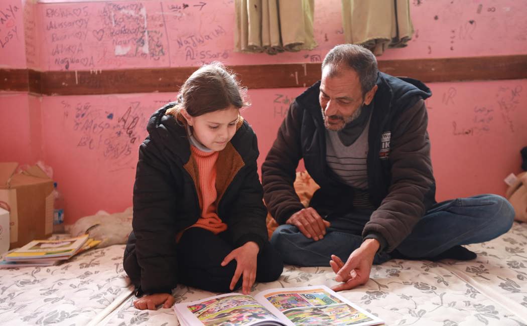 Father-of-three Adnan teaches his daughter Elisia schoolwork at the Mahmoud Saleh school shelter in Jableh city, Latakia Governorate, Syria