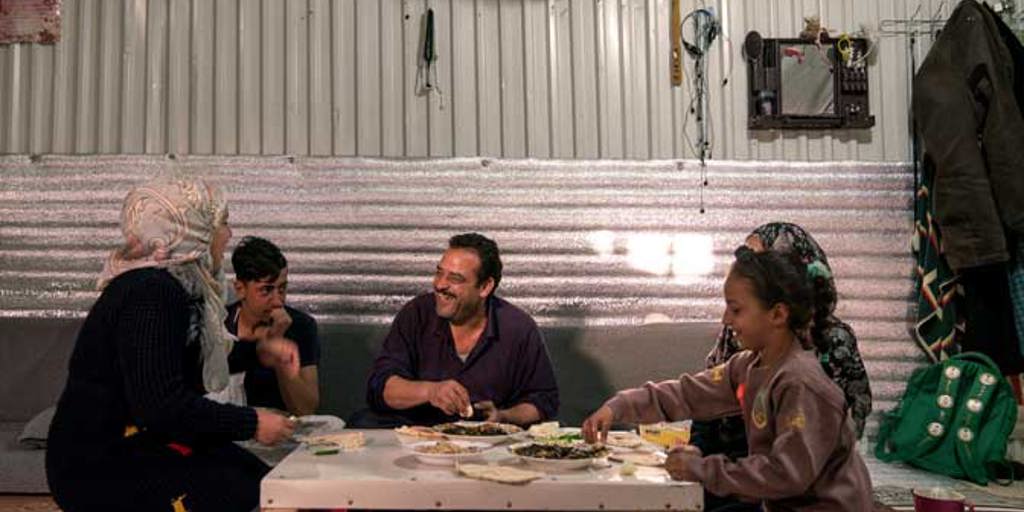 A family gather round a table to eat dinner together at night | Ramadan charity gifts